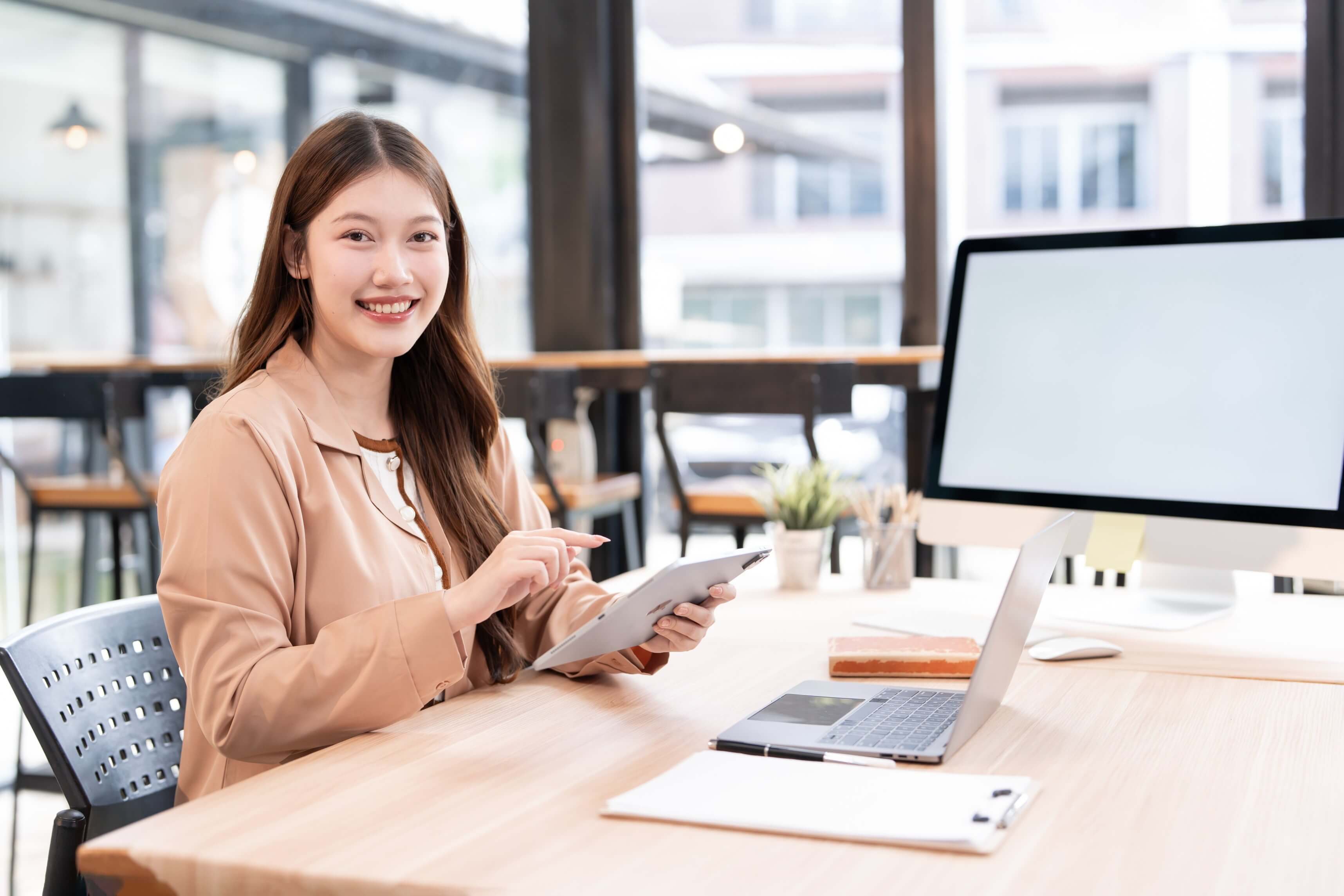 smiling and professional young asian businesswoman using a digital tablet while sitting at her desk