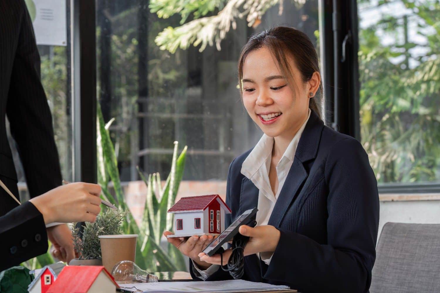 Real estate professional reviewing numbers with a model house and calculator during a client meeting