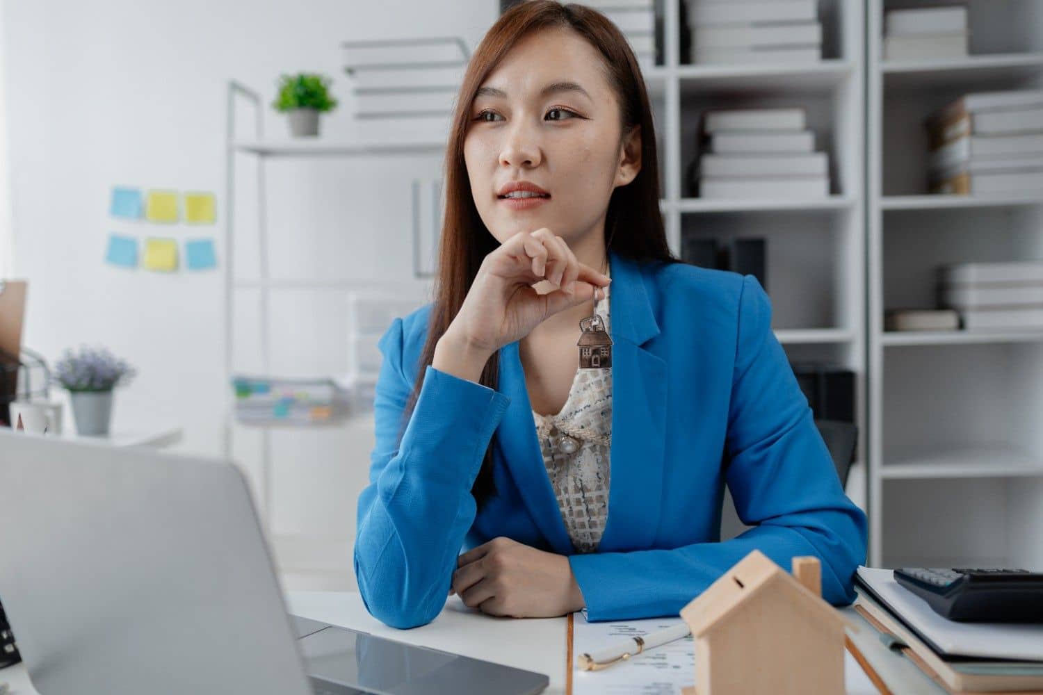 Real estate agent in a blue blazer holding a house-shaped key at her desk