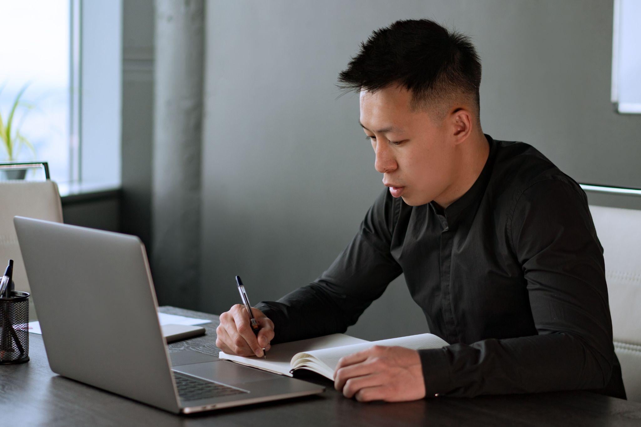 Businessman writing notes laptop desk