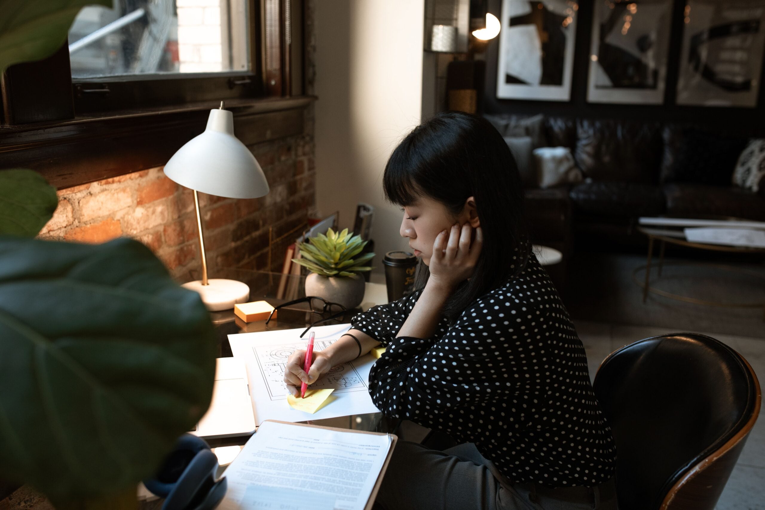Marketing assistant marking up a printed campaign plan with sticky notes at a desk