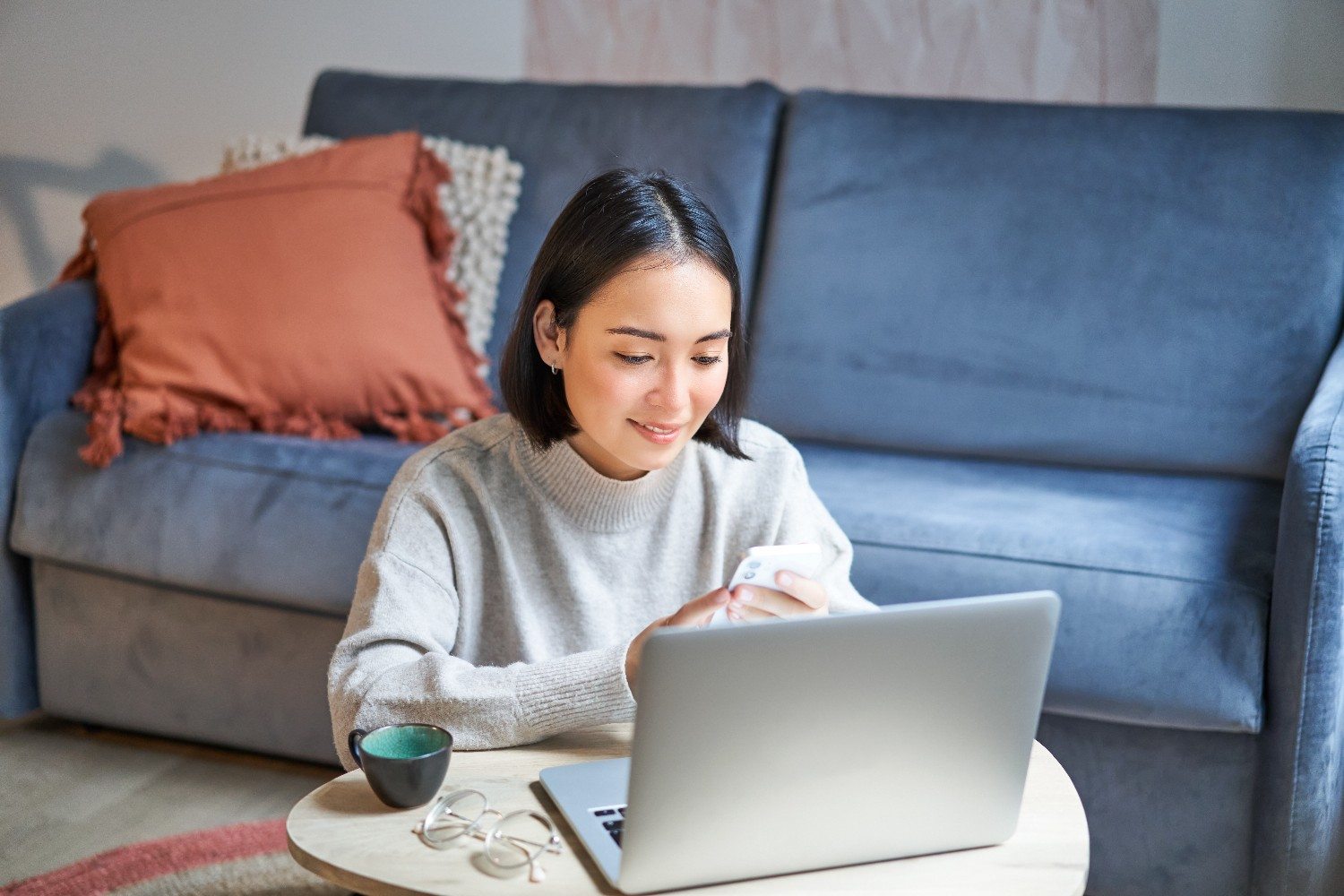 Remote virtual assistant checking her phone at a laptop while working from home