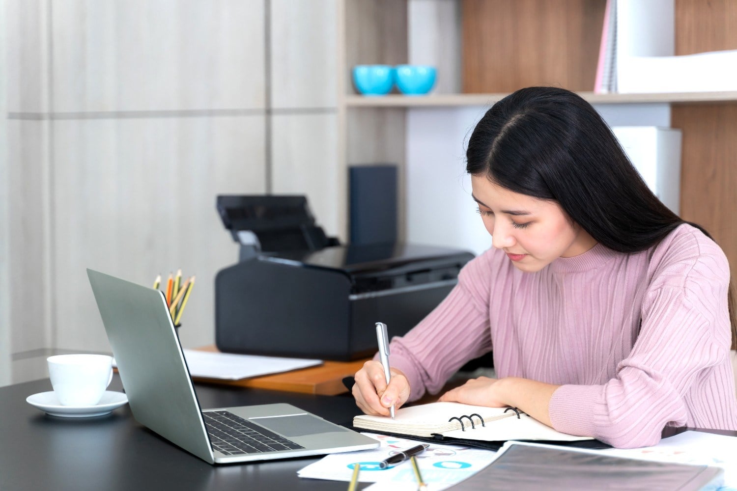 Business owner writing notes beside a laptop while deciding which tasks to delegate