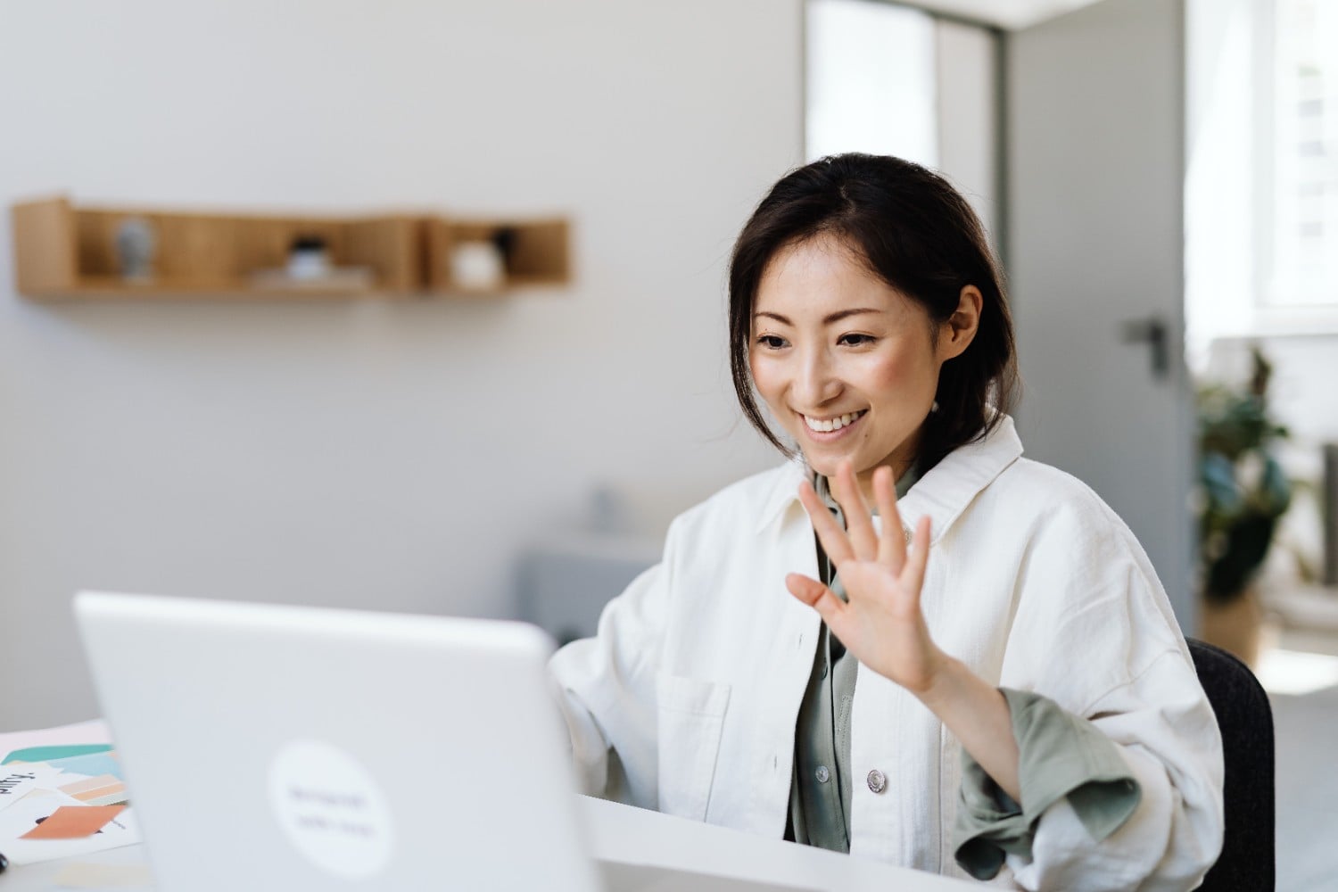 Smiling virtual assistant waving hello on a video call from her desk