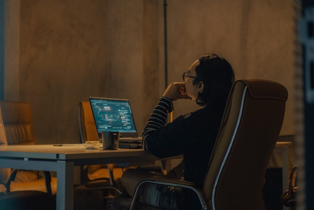 Remote worker reviewing a laptop screen in a dim office during an evening shift