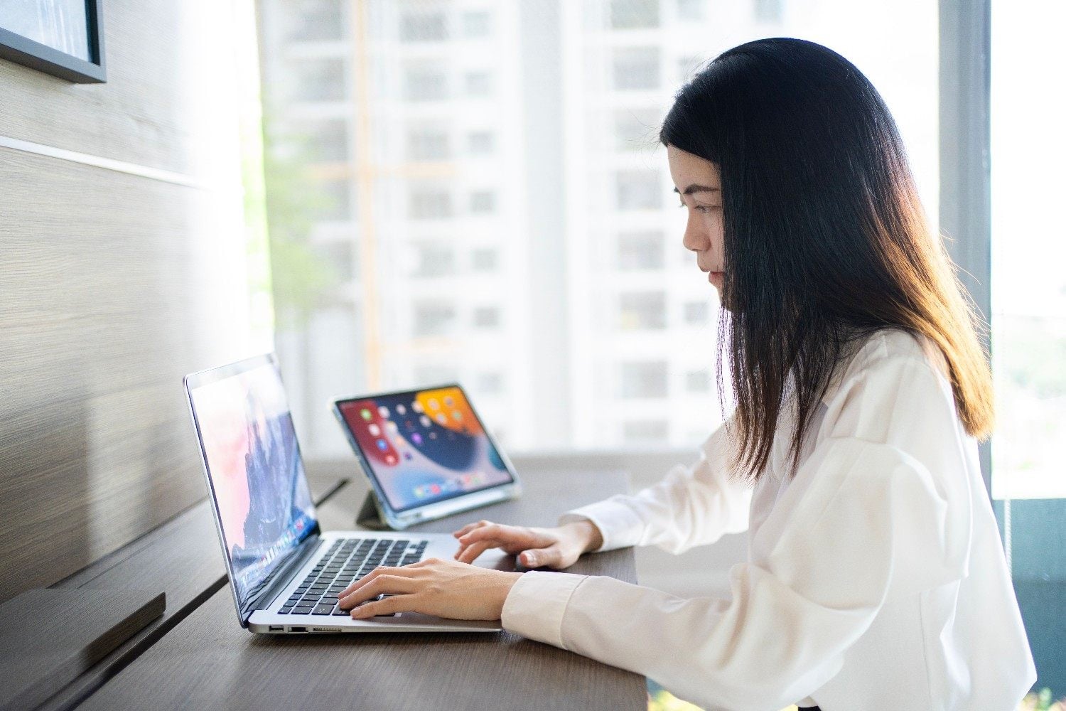 Virtual assistant working on a laptop with a tablet open beside her at a bright desk
